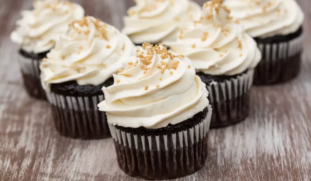 A row of decadent chocolate cupcakes topped with fluffy cool whip and sprinkled with golden brown crumbles, displayed on a wooden surface.