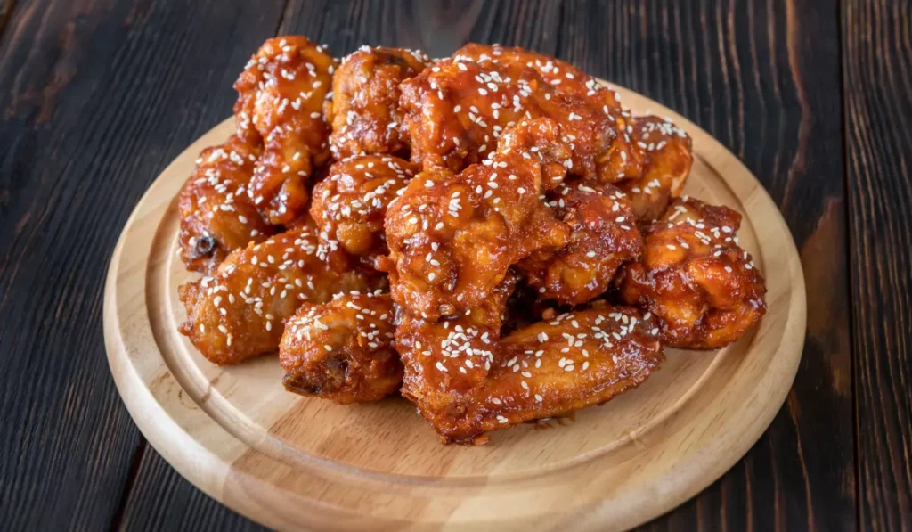 A plate of crispy chicken wings garnished with sesame seeds on a wooden serving board.