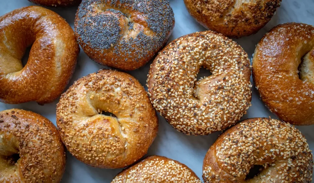Assorted freshly baked bagels with various toppings, including sesame seeds, poppy seeds, and cheese, displayed on a light background. What to put on Asiago bagel?