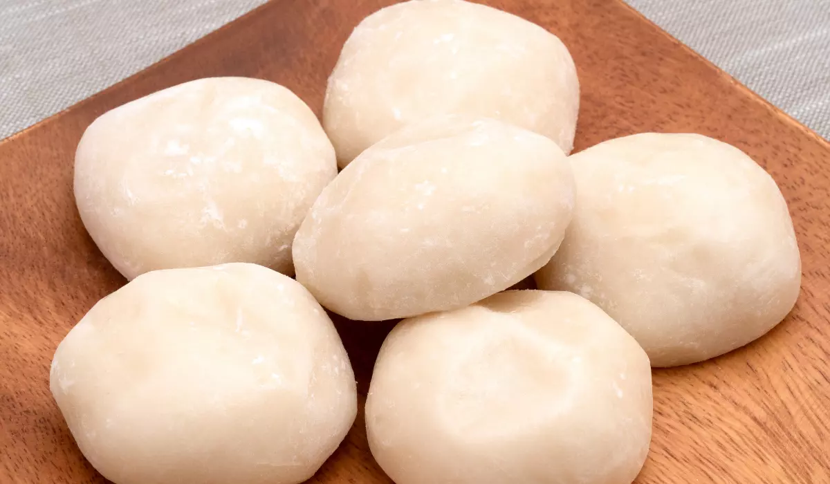 Six pieces of plain mochi displayed on a wooden tray against a linen background.